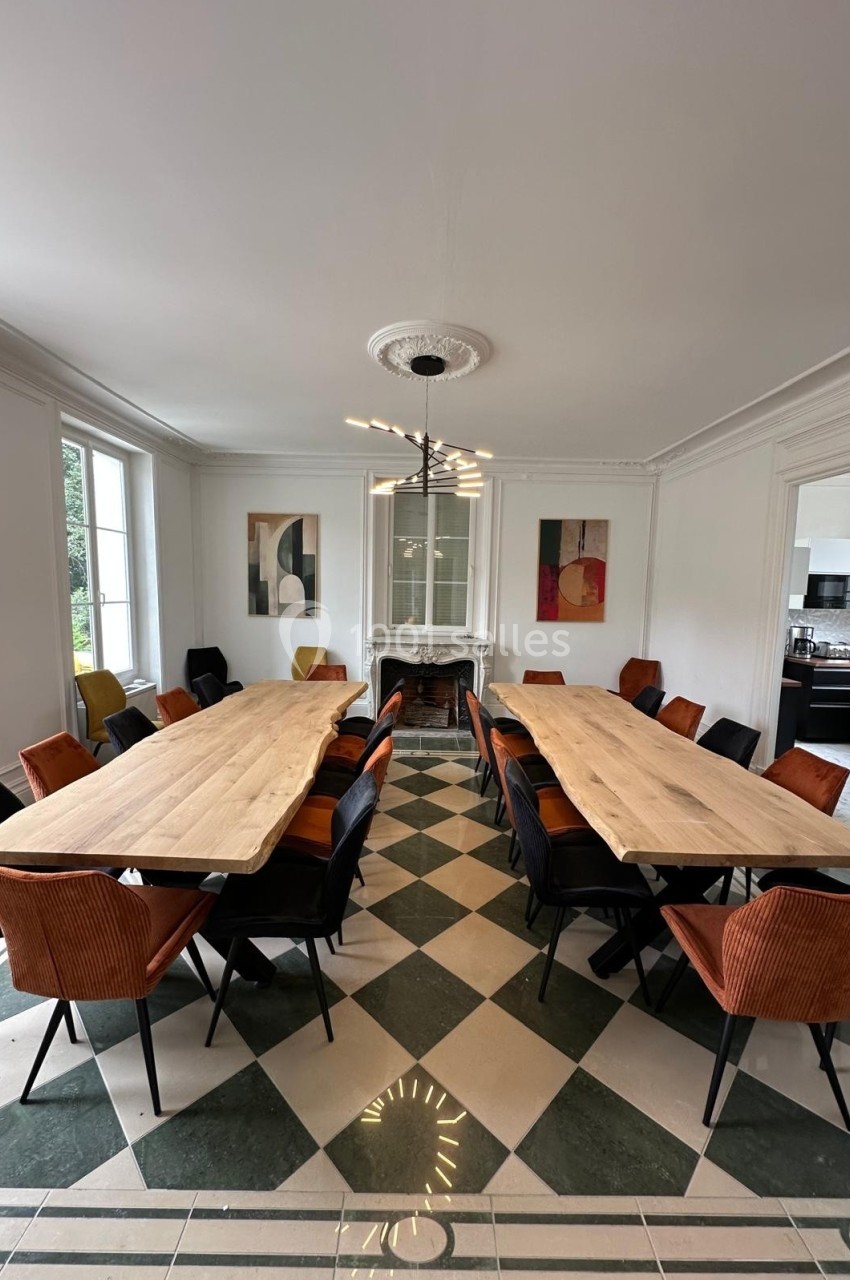 Salle à manger lumineuse avec deux grandes tables en bois, chaises colorées et cheminée décorative au fond.