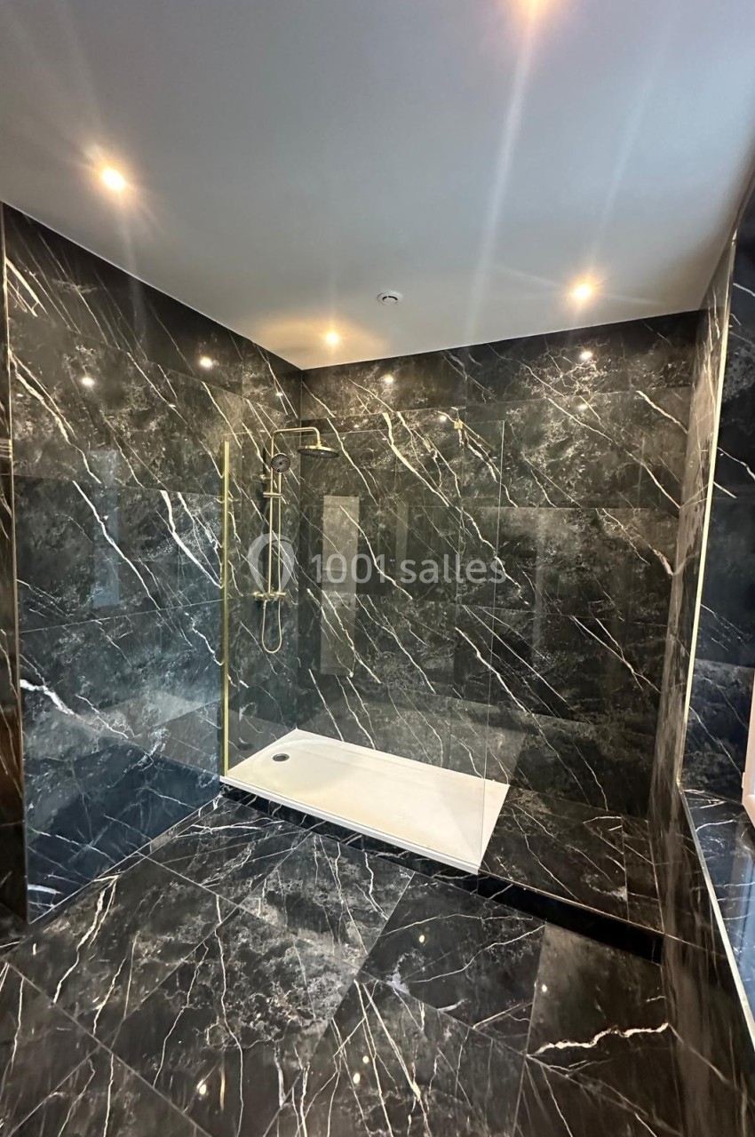 Salle de bain moderne avec murs et sol en marbre noir, douche à l'italienne et paroi vitrée.