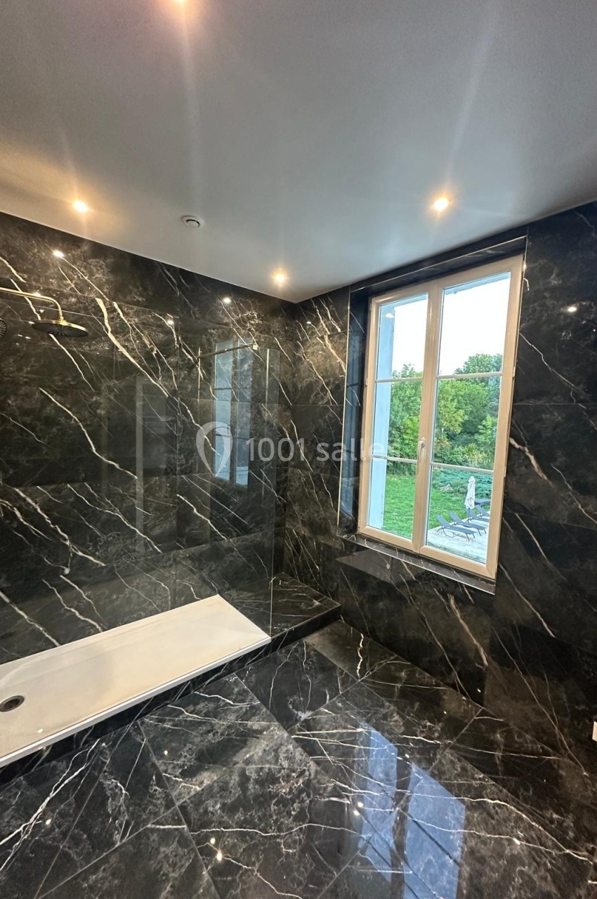 Salle de bain moderne avec murs et sol en marbre noir, douche à l'italienne et fenêtre donnant sur un espace vert.