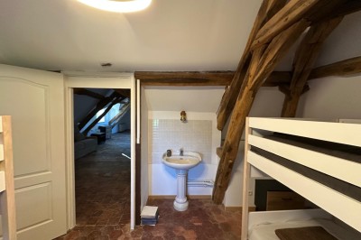 Chambre avec lits superposés en bois, poutres apparentes au plafond et sol en tomettes anciennes.