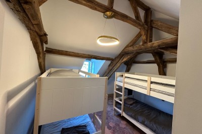 Chambre avec lits superposés en bois, poutres apparentes au plafond et sol en tomettes anciennes.