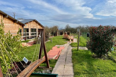 Miniature Location salle Bavent (Calvados) - Domaine des Rouges Terres #9 Allée pavée bordée de verdure, avec un mini-golf et des bâtiments en bois sous un ciel dégagé.