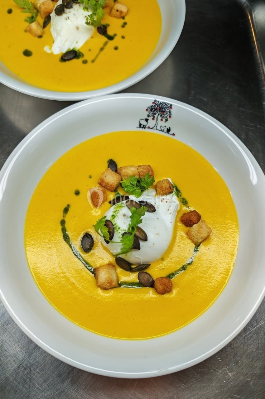 Soupe de potiron garnie de croûtons, graines de courge, crème et herbes fraîches, servie dans une assiette blanche.