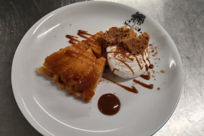 Assiette de dessert composée de mousse, pommes, caramel et crumble, présentée avec soin sur une table sombre.