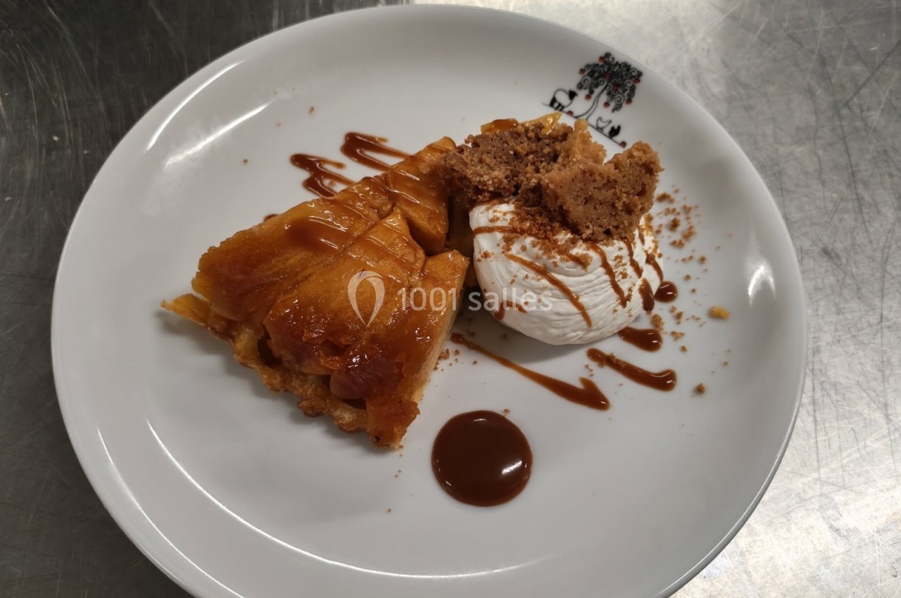 Part de tarte tatin servie avec une boule de glace, crumble et filet de caramel sur une assiette blanche.