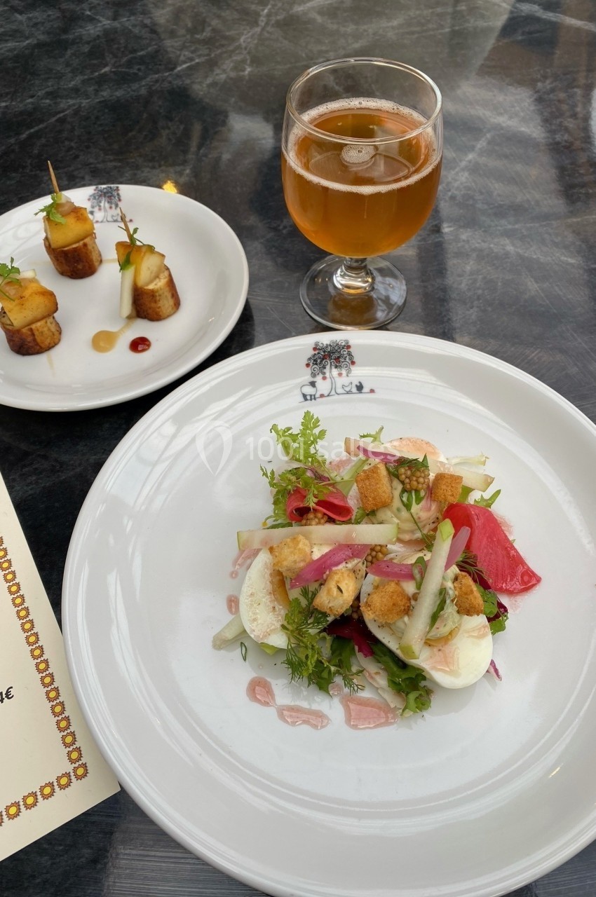 Assiette de salade composée avec œufs, croûtons et légumes, accompagnée de bouchées apéritives et d'un verre de boisson.