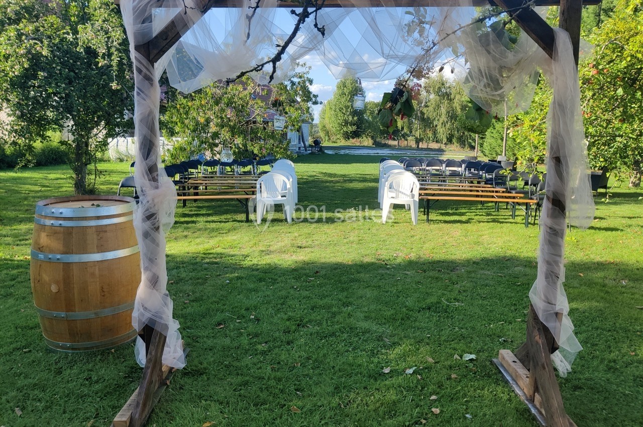 Structure en bois décorée de voilages, avec des chaises et des tables disposées dans un jardin verdoyant.