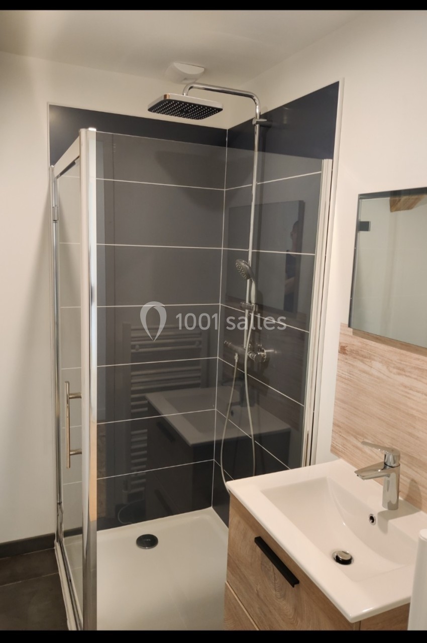 Douche moderne avec paroi vitrée, pommeau de douche carré, lavabo blanc et meuble en bois clair.