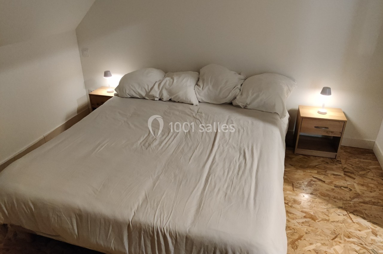 Lit double avec draps blancs, encadré par deux tables de chevet en bois avec lampes allumées, sur un sol en bois clair.