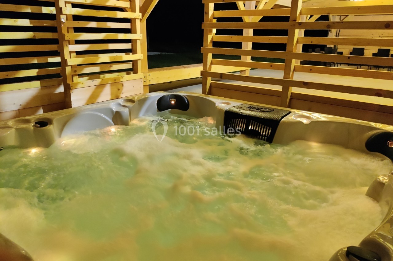 Un jacuzzi bouillonnant installé sous une structure en bois, éclairé dans un environnement nocturne.