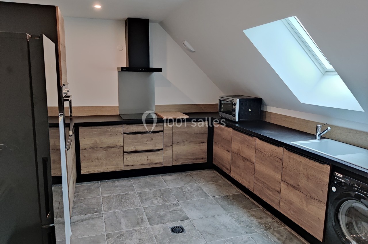 Cuisine moderne sous combles avec meubles en bois, plan de travail noir, électroménagers intégrés et fenêtre de toit.