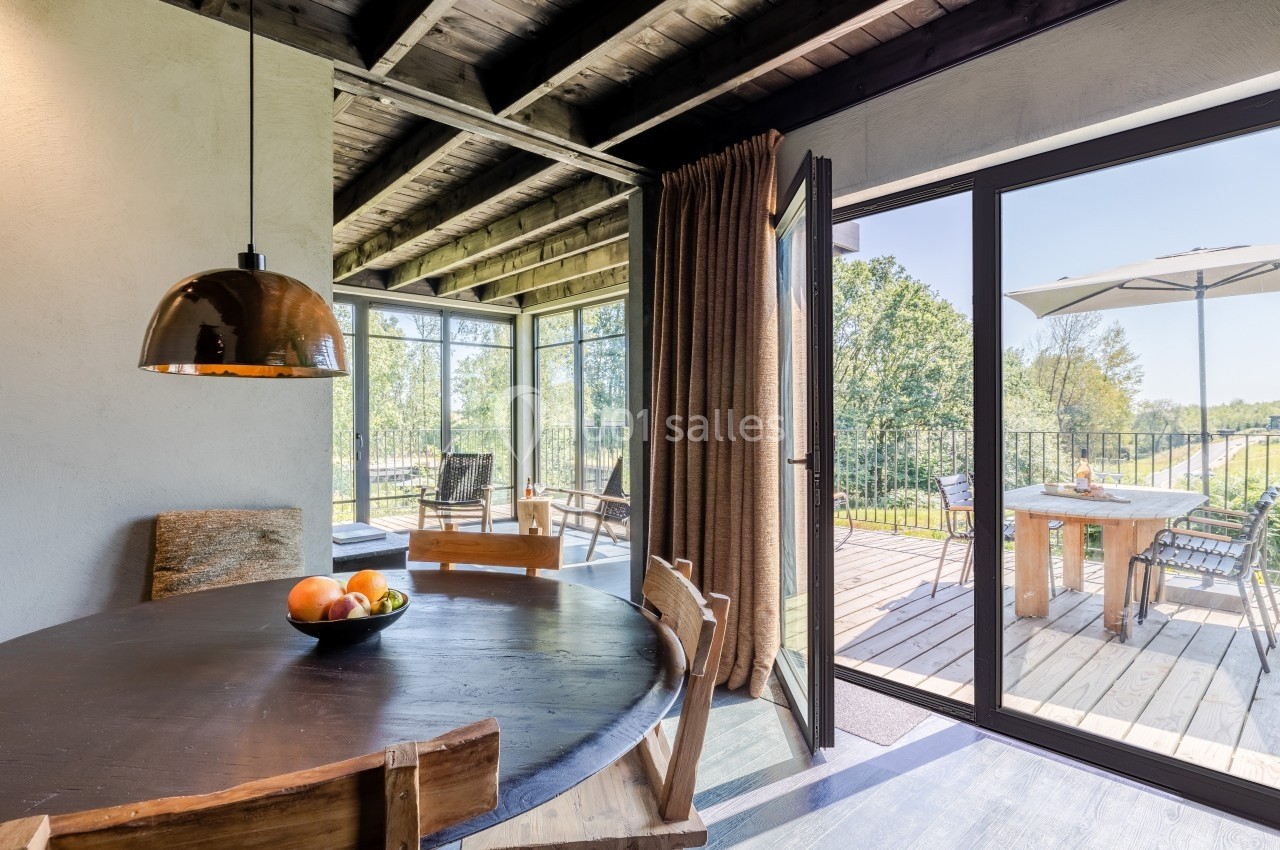 Salle à manger lumineuse avec table en bois, vue sur une terrasse ensoleillée équipée de mobilier extérieur.