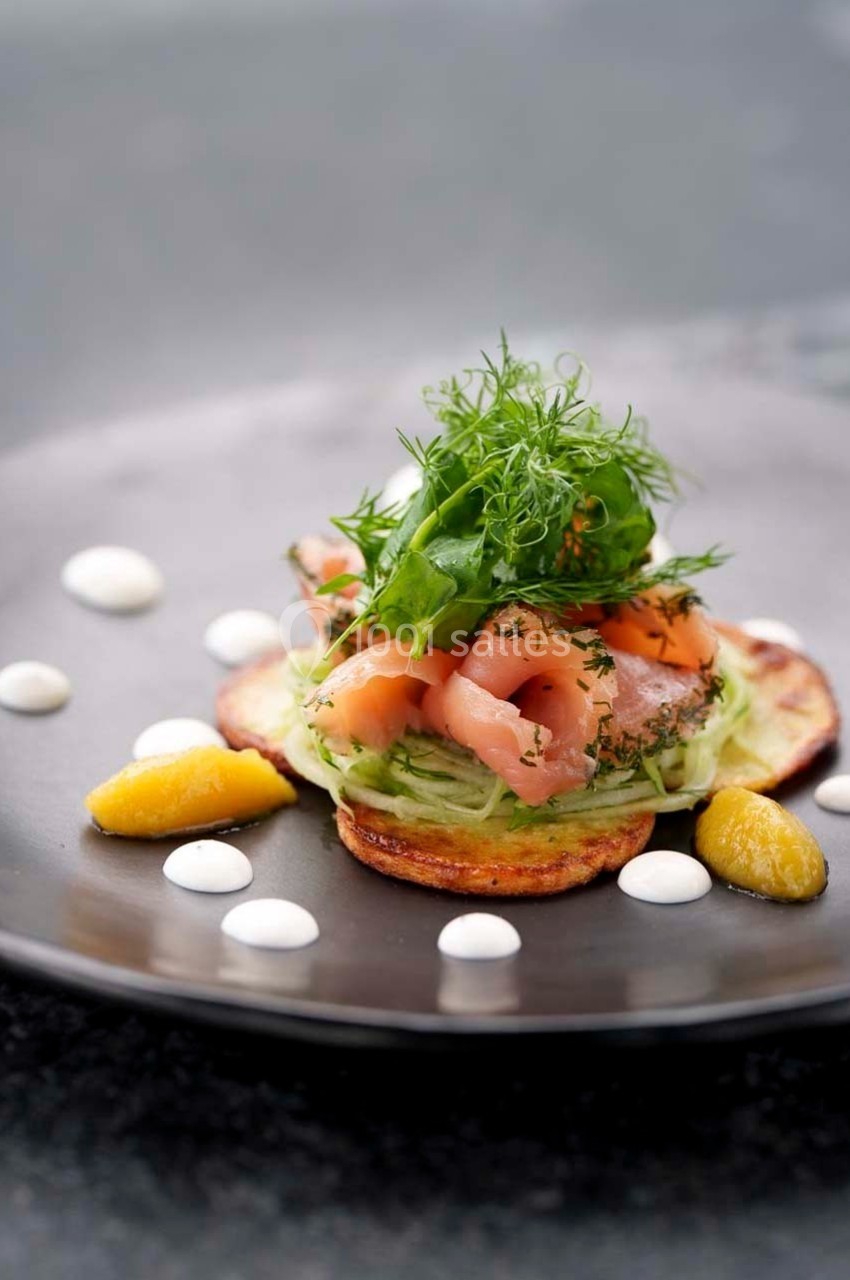 Assiette garnie de saumon fumé, légumes frais, herbes et sauce, présentée sur une base de galette de pomme de terre.