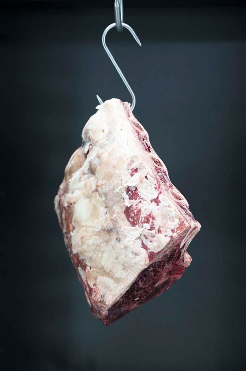 Morceau de viande crue suspendu à un crochet métallique dans un environnement sombre.