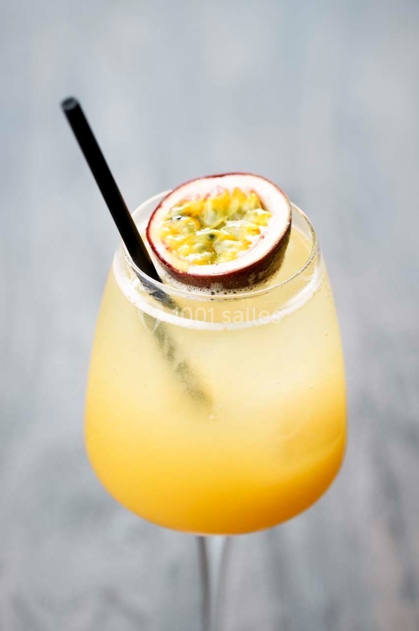 Verre de cocktail jaune garni d'une demi-passion et d'une paille noire sur fond flou.