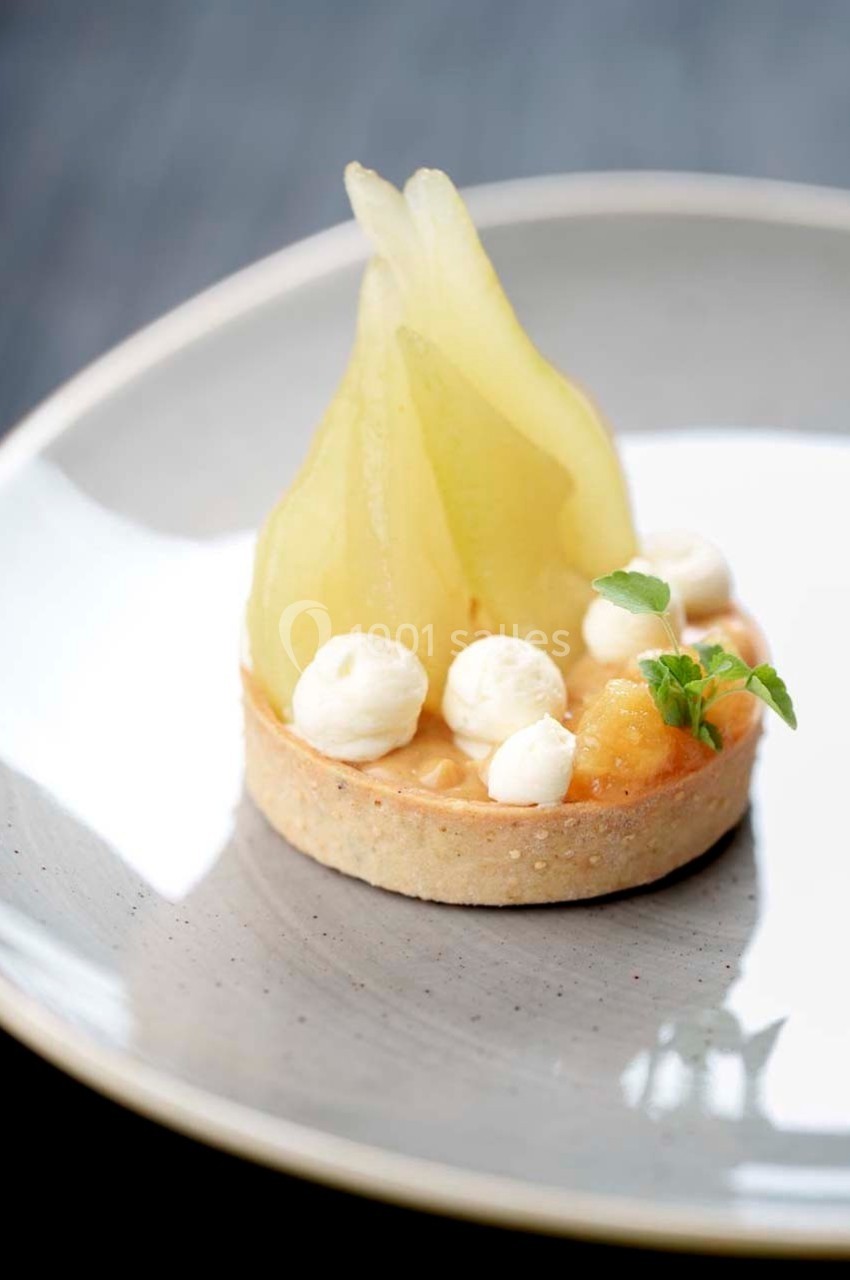 Tartelette garnie de poires pochées, crème et décorée de petites touches de chantilly sur une assiette grise.