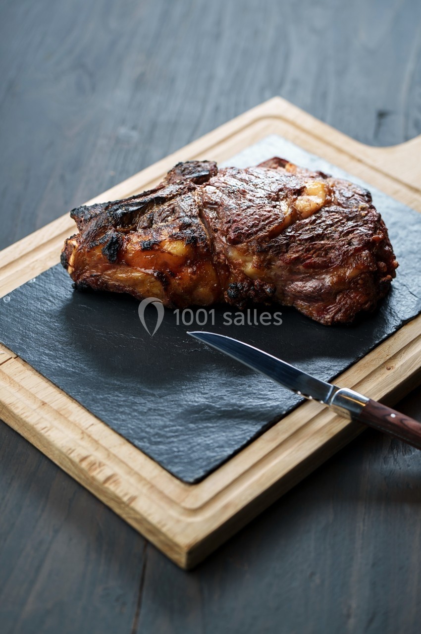 Côte de bœuf grillée posée sur une planche en ardoise avec un couteau à côté.