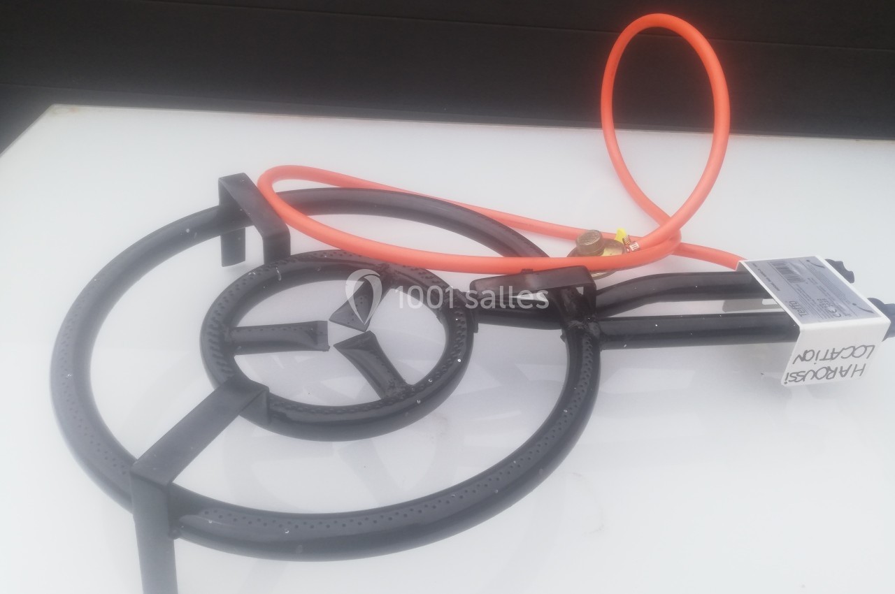 Brûleur à gaz en métal noir avec tuyau orange et régulateur, posé sur une surface blanche.