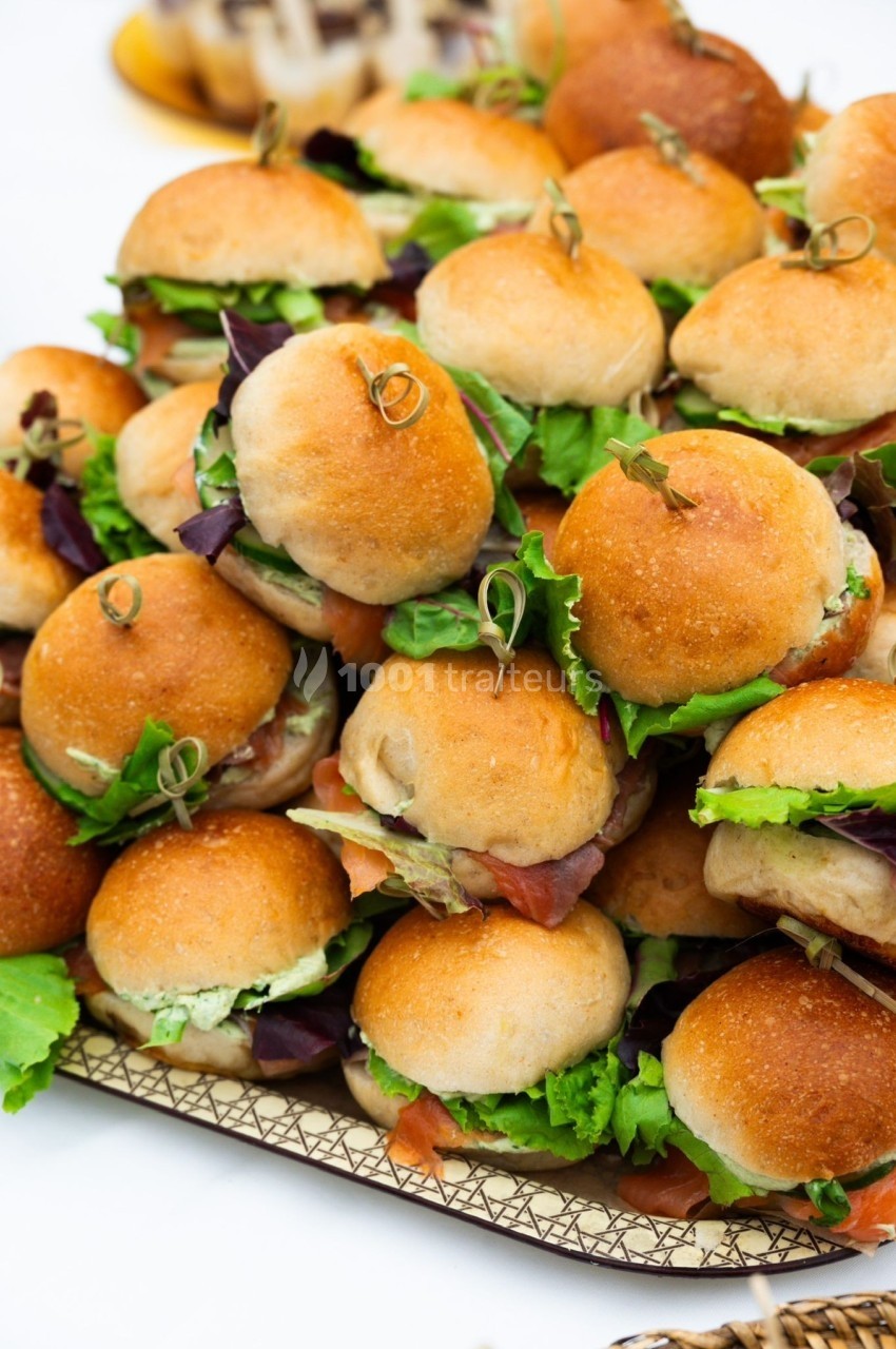 Plateau de mini-burgers garnis de salade et de charcuterie, présentés sur un support en bois.