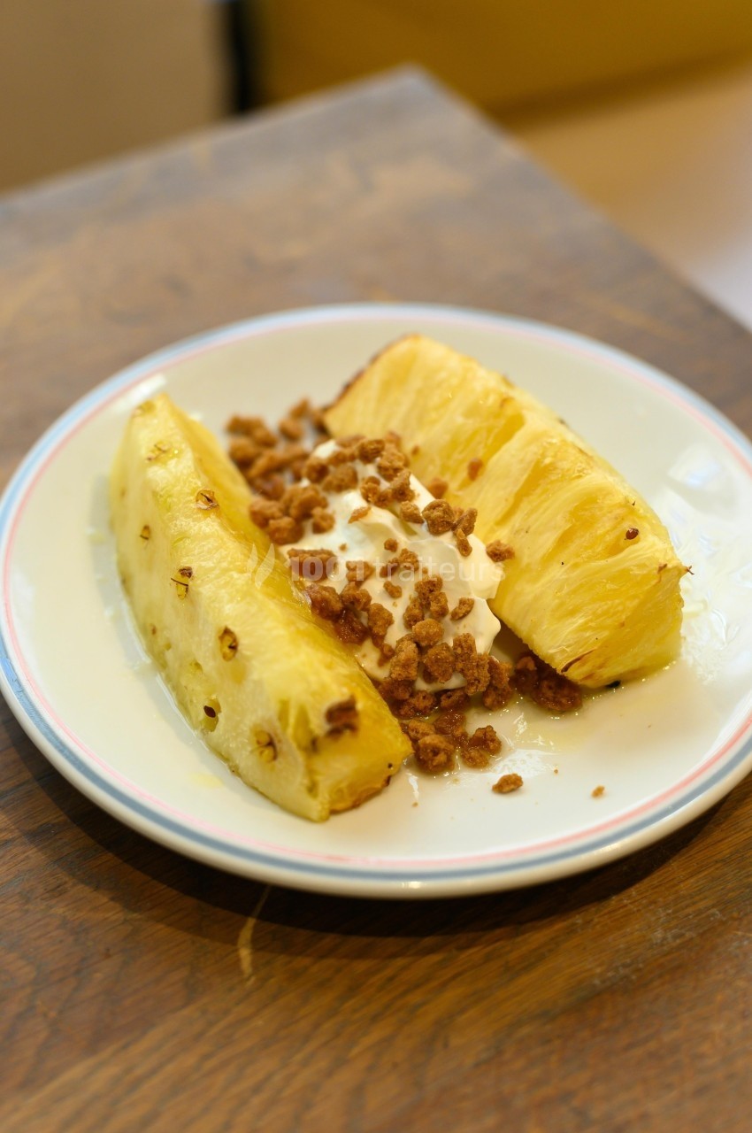 Tranches d'ananas frais servies avec une garniture de crème et des éclats de noix sur une assiette blanche.