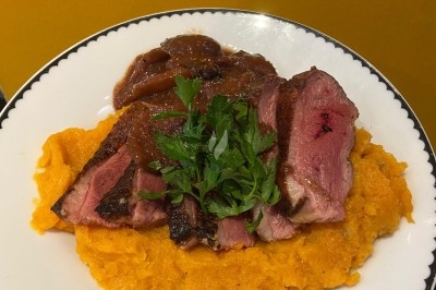 Assiette de magret de canard tranché sur purée de patates douces, garni de persil et accompagné d'une sauce.