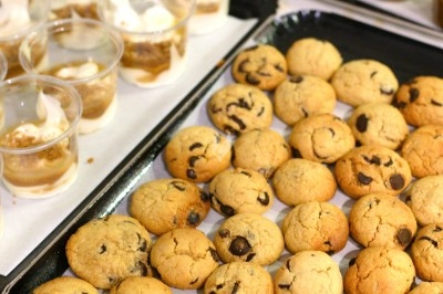 Plateaux de cookies aux pépites de chocolat et verrines de dessert disposés sur une table.