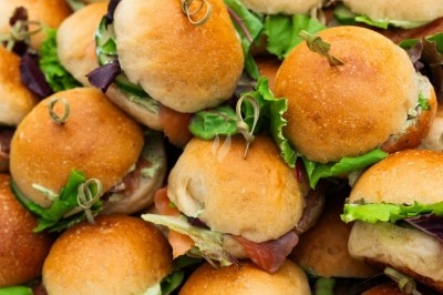 Plateau de mini-burgers garnis de salade et de charcuterie, présentés sur un support en bois.