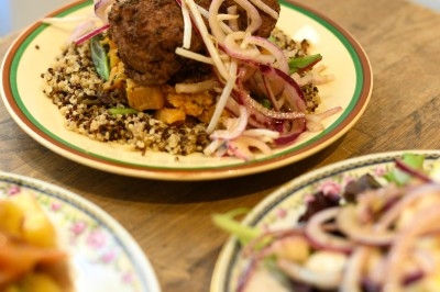 Assiette de viande servie sur un lit de quinoa avec légumes et oignons rouges, posée sur une table en bois.