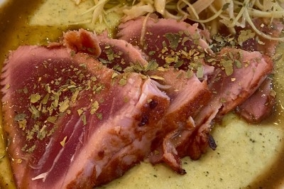 Assiette de magret de canard tranché sur purée de patates douces, garni de persil et accompagné d'une sauce.