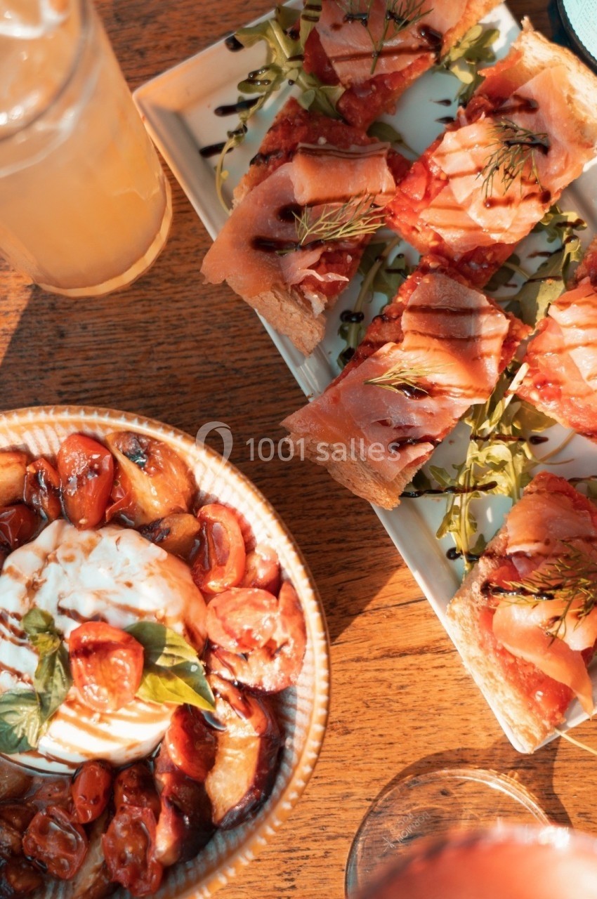 Assortiment de bruschettas au jambon et burrata avec tomates cerises, présenté sur une table en bois.