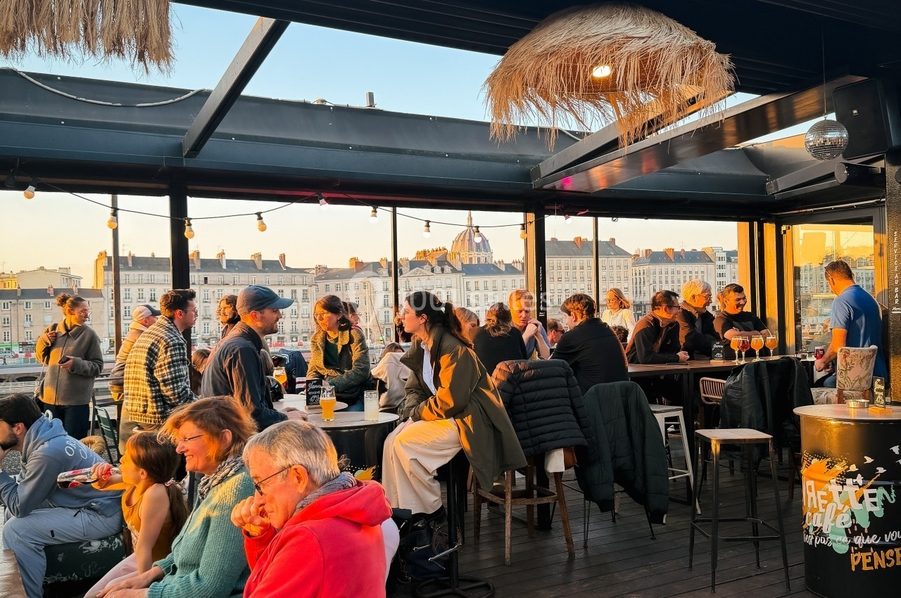 Groupe de personnes discutant et partageant un moment convivial sur une terrasse ensoleillée avec vue sur des bâtiments.