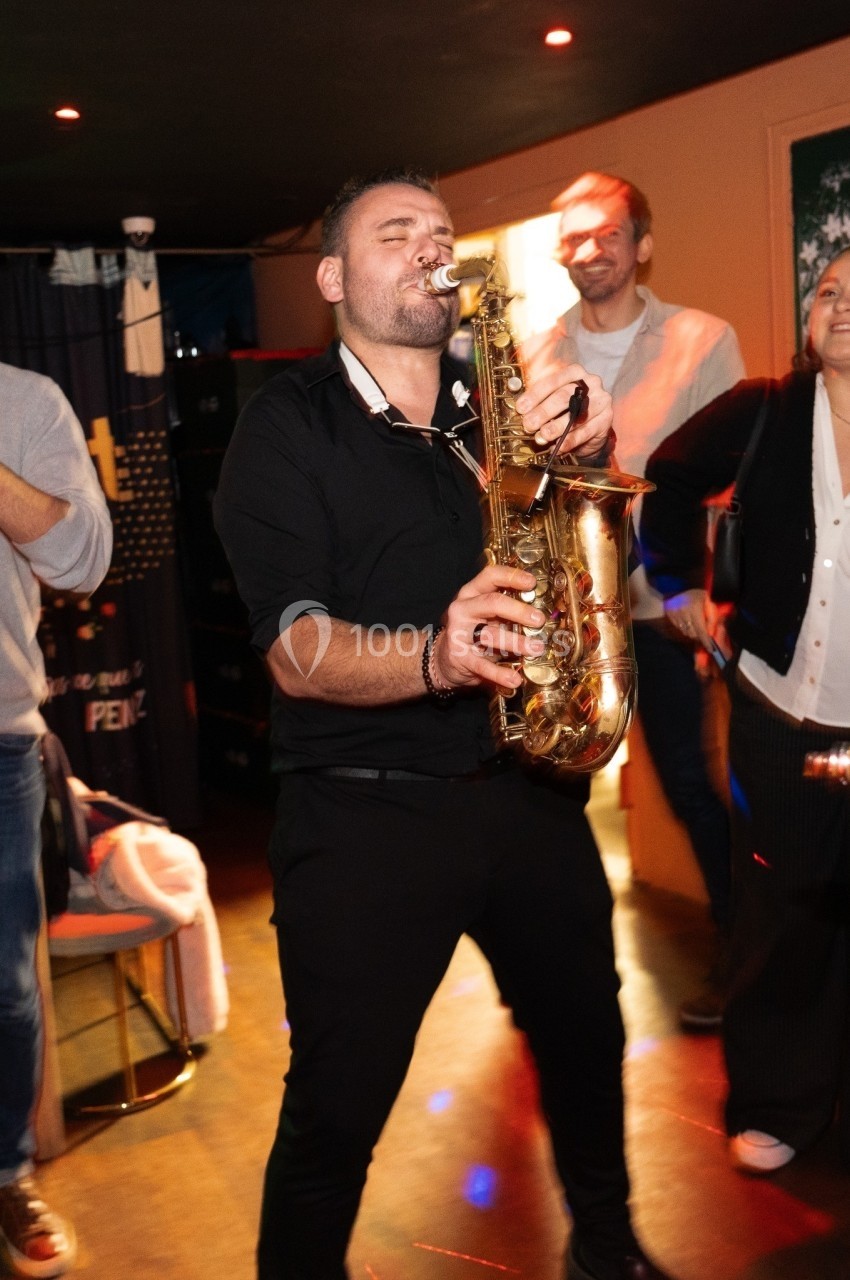 Un musicien joue du saxophone dans une ambiance festive, entouré de personnes souriantes.
