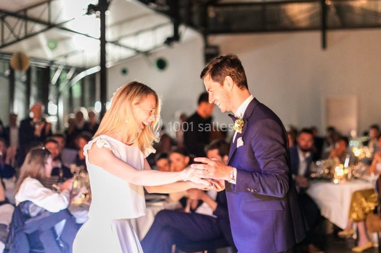 Un couple danse lors d'une réception dans une salle éclairée, entouré d'invités assis à des tables.