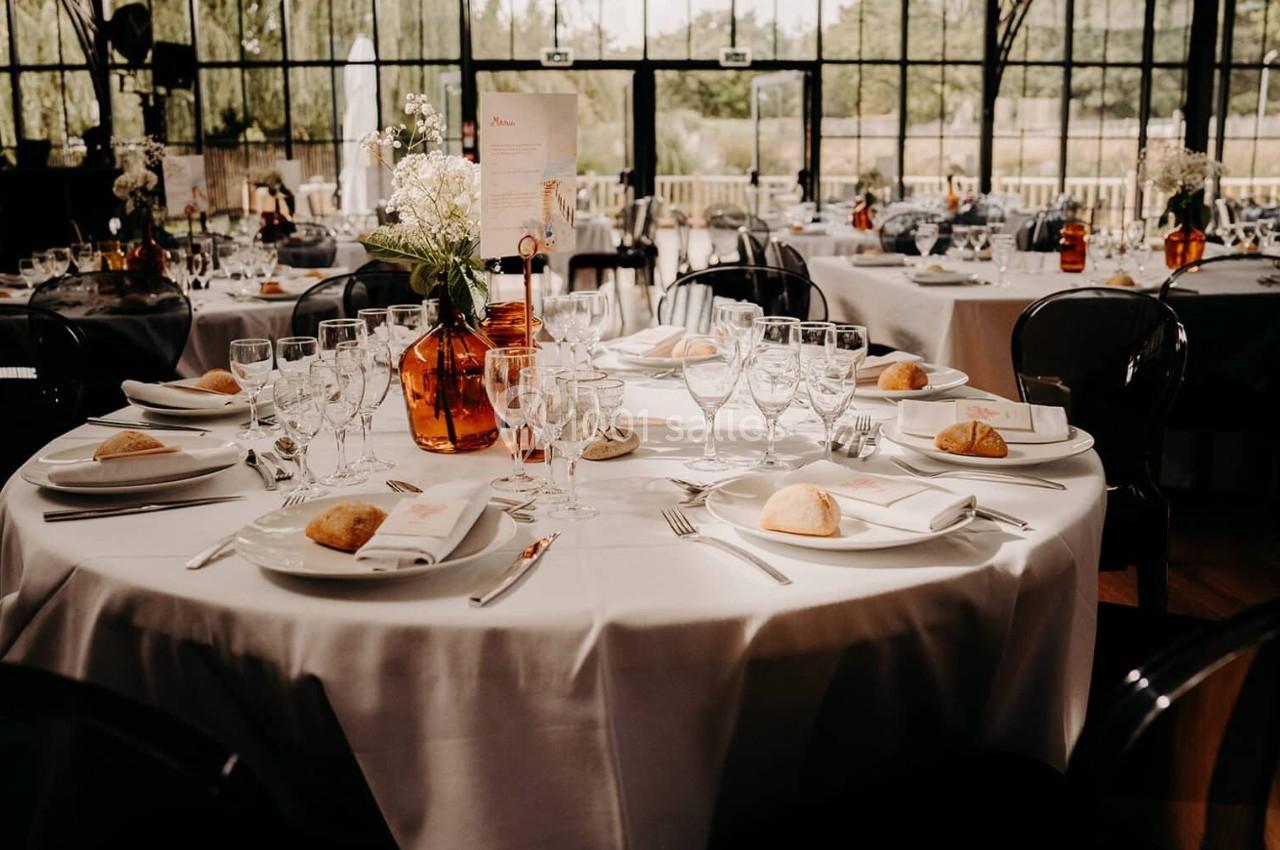 Tables de réception élégamment dressées avec nappes blanches, vaisselle, verres et décorations florales.