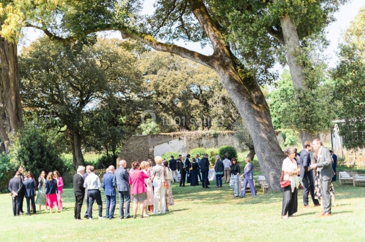 Des personnes rassemblées dans un jardin arboré lors d'un événement en plein air par une journée ensoleillée.