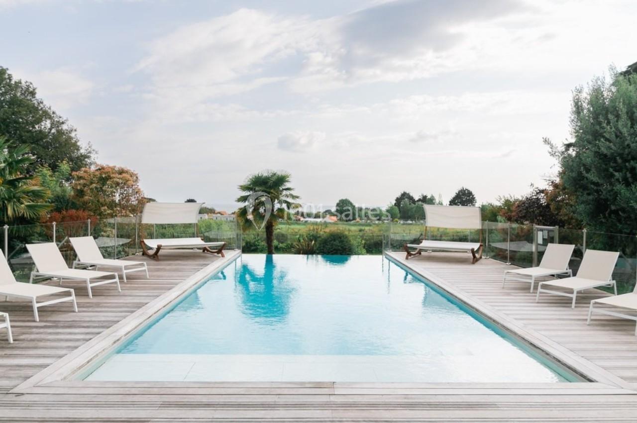 Piscine extérieure entourée de chaises longues et de végétation, avec vue sur un paysage verdoyant.