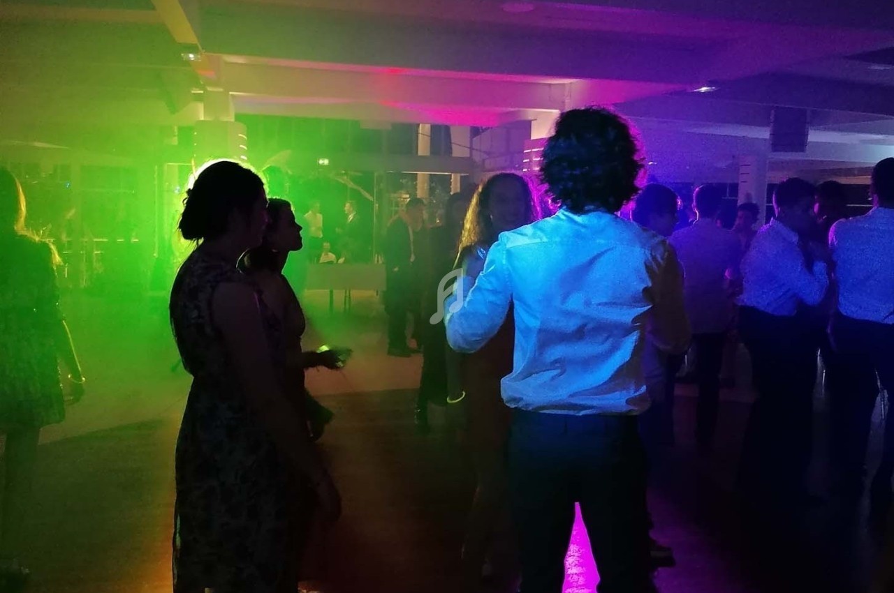 Personnes dansant dans une salle éclairée par des lumières colorées, créant une ambiance festive.