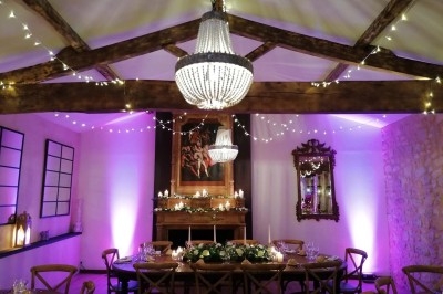 Salle décorée pour un dîner, avec table dressée, guirlandes lumineuses, lustres et éclairage d'ambiance violet.