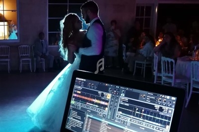 Un couple danse lors d'une réception de mariage, avec une table de mixage visible au premier plan.