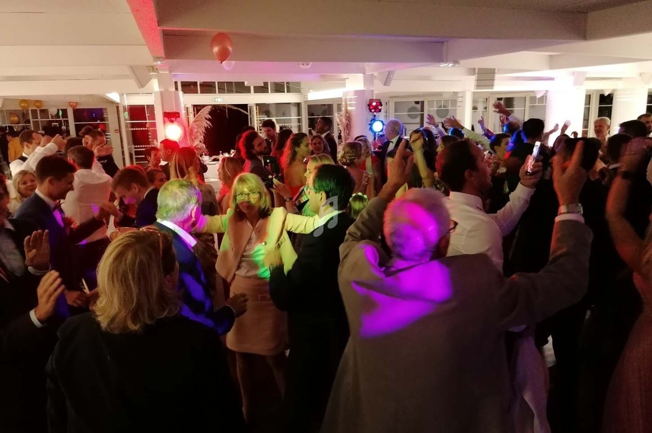 Groupe de personnes dansant dans une salle éclairée par des lumières colorées lors d'un événement festif.