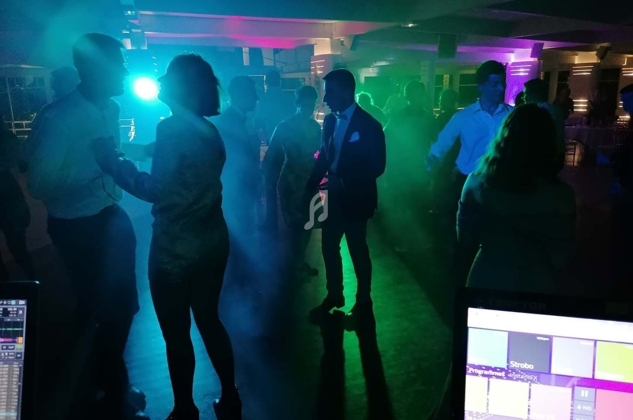 Personnes dansant dans une salle sombre éclairée par des lumières colorées et un écran de contrôle visible au premier plan.