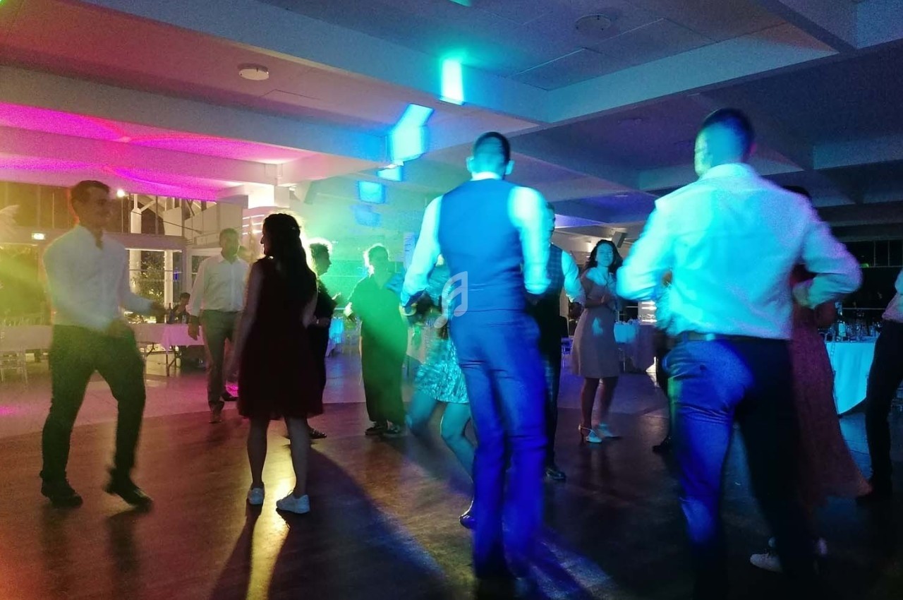 Personnes dansant sous des lumières colorées dans une salle de réception en soirée.