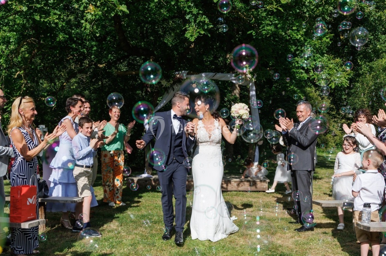 Un couple de mariés marche sous des bulles de savon, entouré d'invités applaudissant dans un jardin verdoyant.
