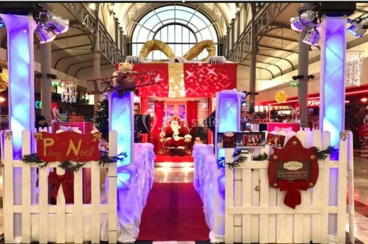 Décoration de Noël dans un centre commercial avec Père Noël, cadeaux géants, ours en peluche et éclairages festifs.