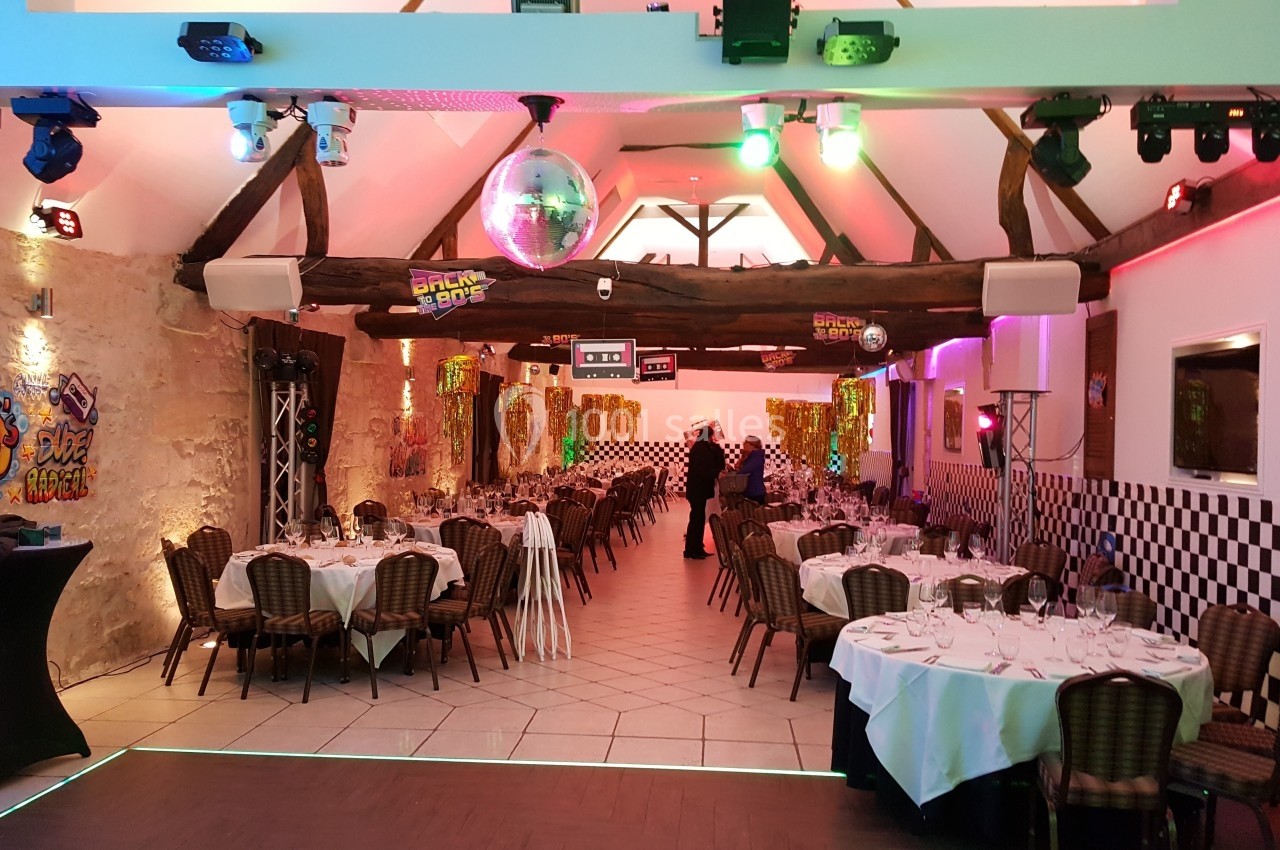 Salle décorée sur le thème des années 80 avec tables dressées, éclairages colorés et éléments rétro.