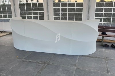 Comptoir blanc au design ondulé installé sous une tente avec sol en dalles grises et murs translucides.