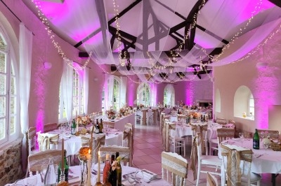 Salle de réception décorée avec des guirlandes lumineuses, nappes blanches et éclairage rose, tables dressées pour un…