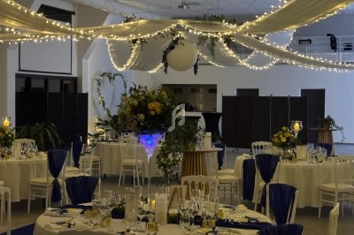 Salle de réception décorée avec des guirlandes lumineuses, des tables rondes dressées et des arrangements floraux jaunes et…
