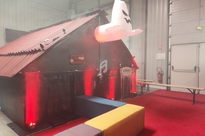 Maison hantée décorée avec des lumières rouges, un fantôme gonflable blanc suspendu et des accessoires effrayants.