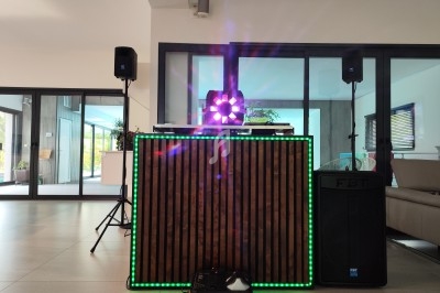 Console de DJ en bois avec éclairage LED coloré, entourée de haut-parleurs dans une pièce moderne.